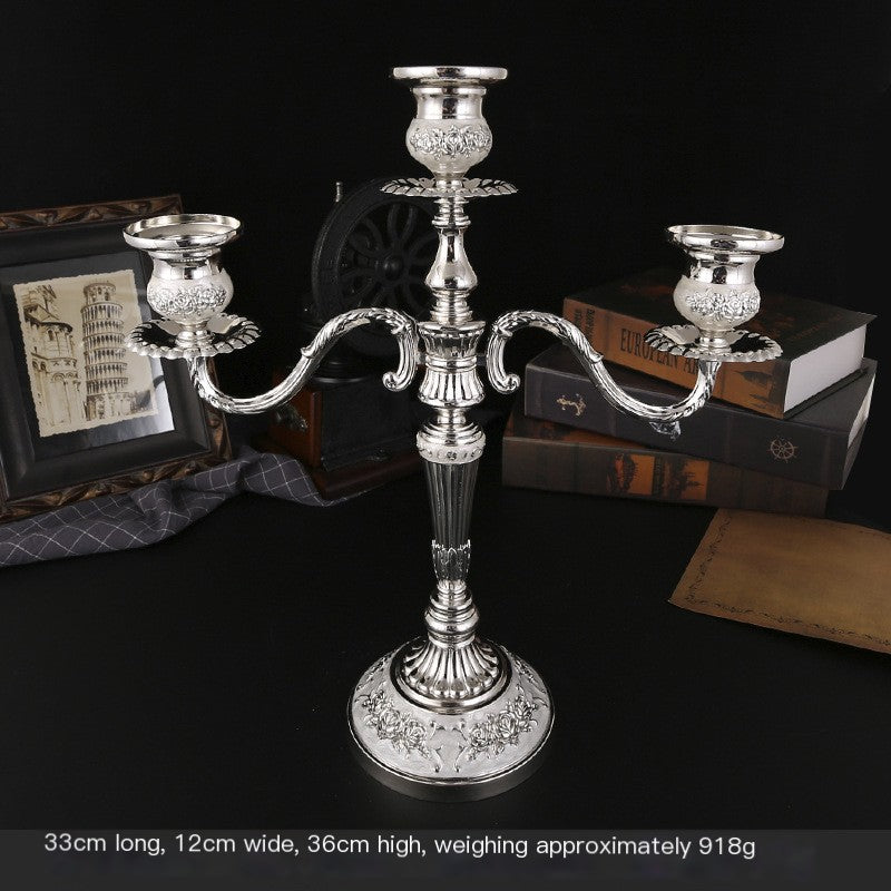 Silver candelabra on a dark surface with books and a framed picture in the background