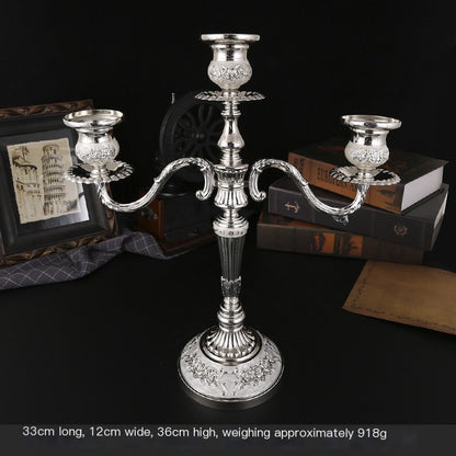 Silver candelabra on a dark surface with books and a framed picture in the background