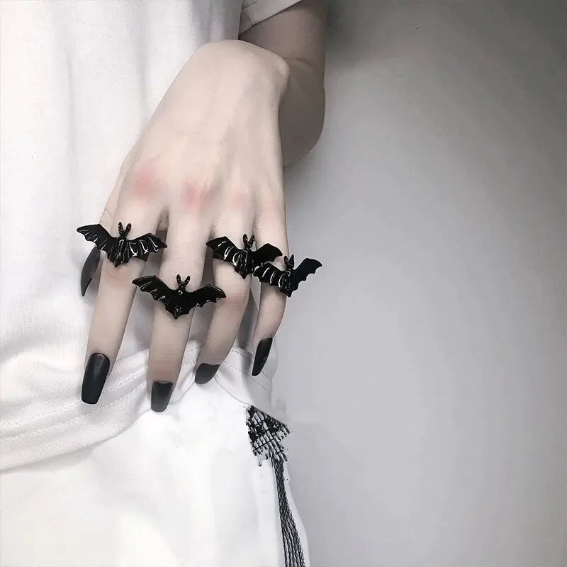 Hand wearing black bat-shaped rings on a plain background