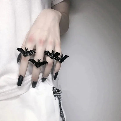 Hand wearing black bat-shaped rings on a plain background