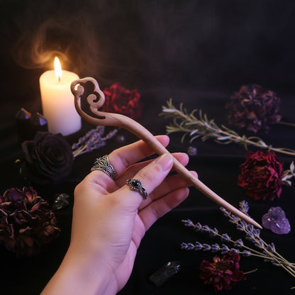 Hand holding a wooden hairpin against a black background