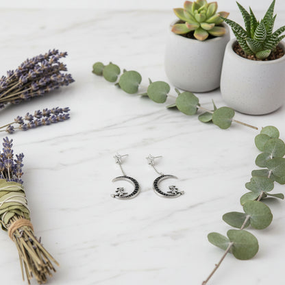 Pair of silver earrings with crescent moon and star designs on a white background