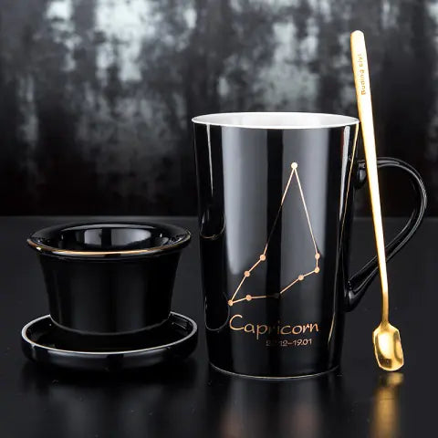 Black mug with Capricorn zodiac design, gold spoon, and small black cup on a dark background