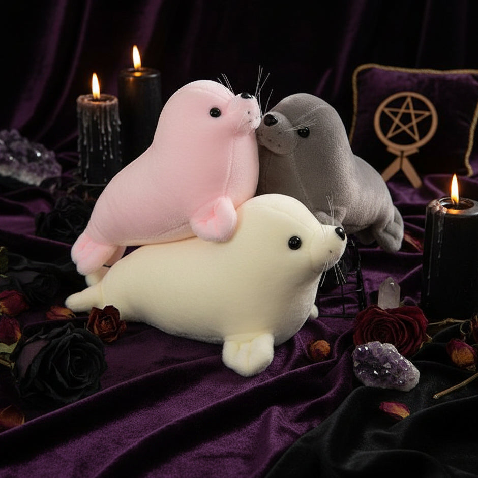 Three plush seal toys in pink, gray, and white on a textured surface with a blurred background.