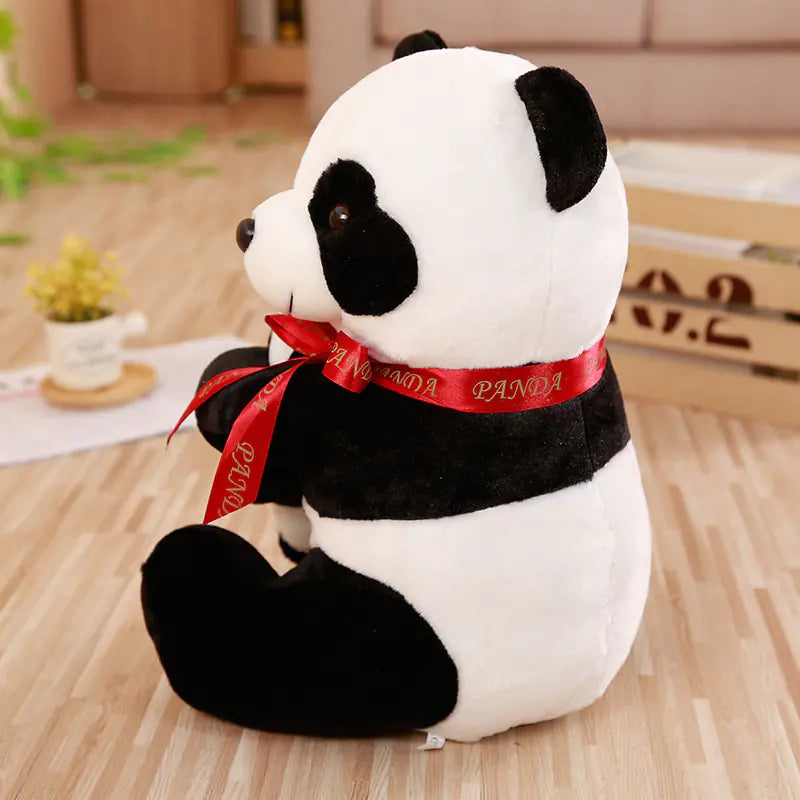 Plush panda toy with a red ribbon on a wooden floor.