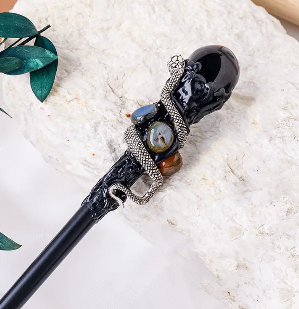Decorative obsidian crystal magic wand with black handle and decorative elements on a white surface
