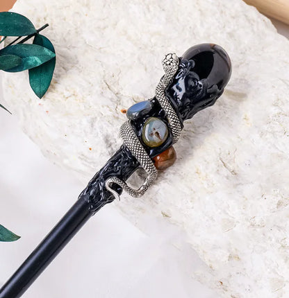 Decorative obsidian crystal magic wand with black handle and decorative elements on a white surface