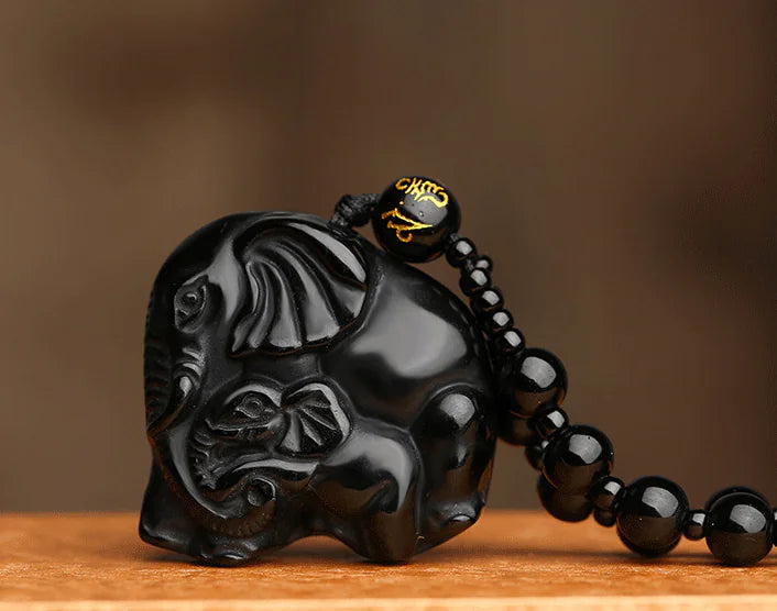 Black carved elephant pendant with chain on a wooden surface