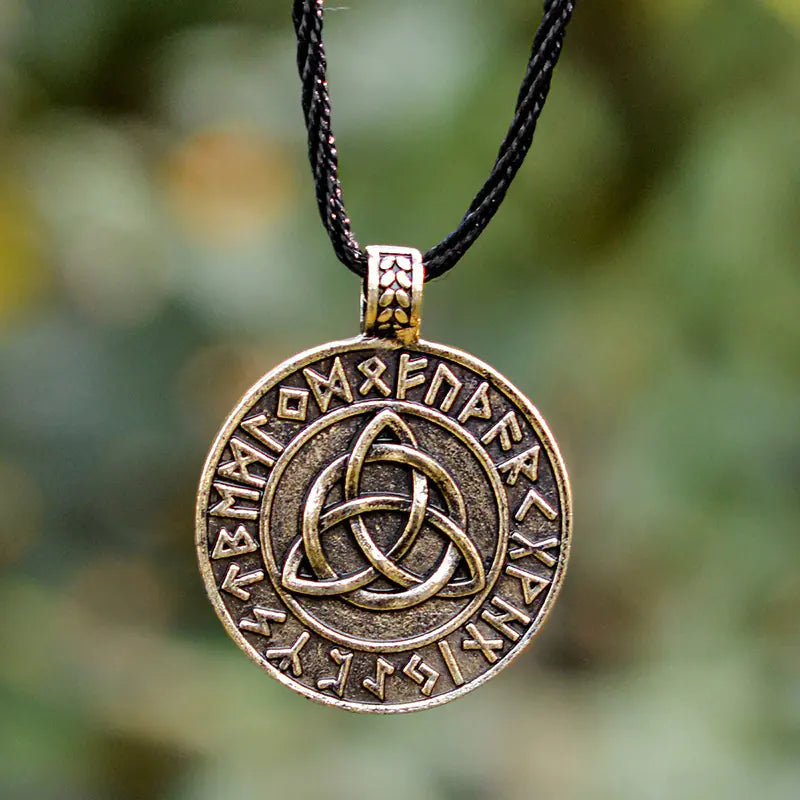 Bronze pendant with Celtic knot design and runic text on a black cord against a blurred green background