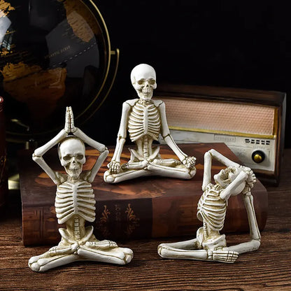 Three skeleton figurines in yoga poses on a wooden surface with a radio in the background.