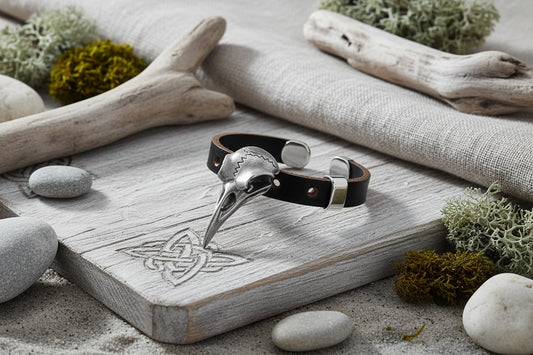 Bracelet with silver skull charm and brown leather strap on a dark background