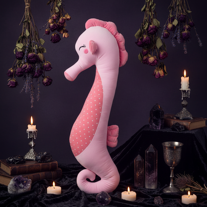 Pink plush seahorse toy on a light wooden floor with a white crib and blue curtains in the background.