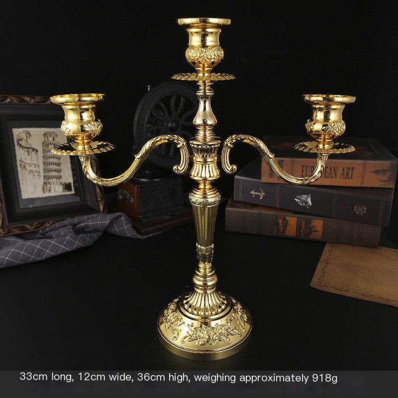 Gold candle holder on a dark surface with books and decorative items in the background