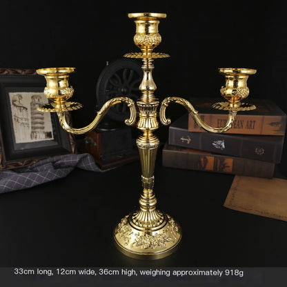 Gold candle holder on a dark surface with books and decorative items in the background