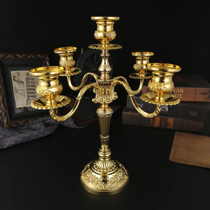 Gold candelabrum on a dark surface with books and a picture frame in the background