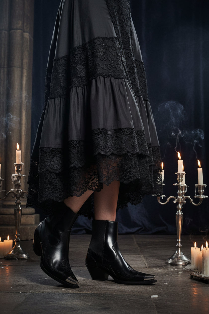 Black leather ankle boots with metallic accents worn by a person on a white background