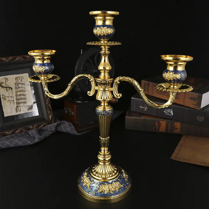 Decorative gold and blue candle holder on a dark surface with books and a framed picture in the background.