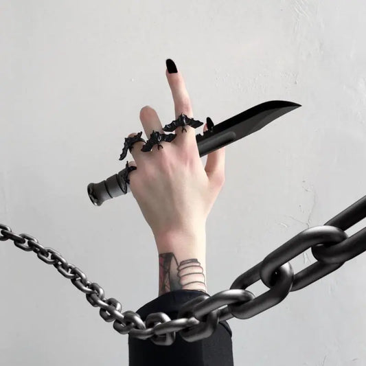 Hand holding a black knife with multiple rings and tattoos, surrounded by chains on a light gray background