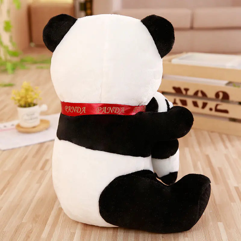 Plush panda toy with a red ribbon on a wooden floor.