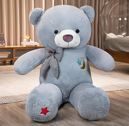 Large blue teddy bear with a bow tie and star patch on a wooden floor.