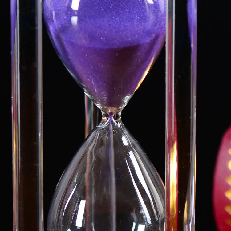 Close-up of a sand timer with purple sand against a black background