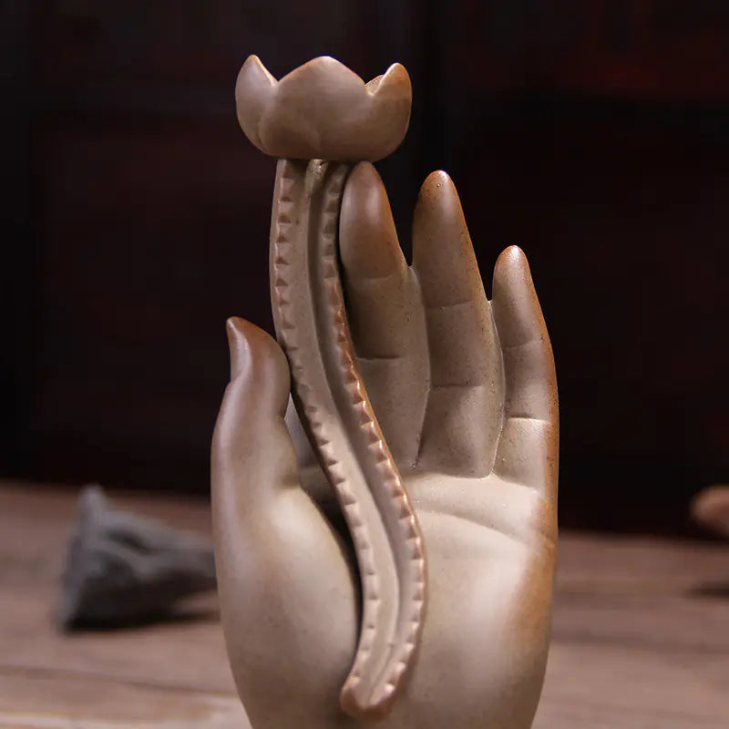Ceramic sculpture of a hand holding a lotus flower on a wooden surface.