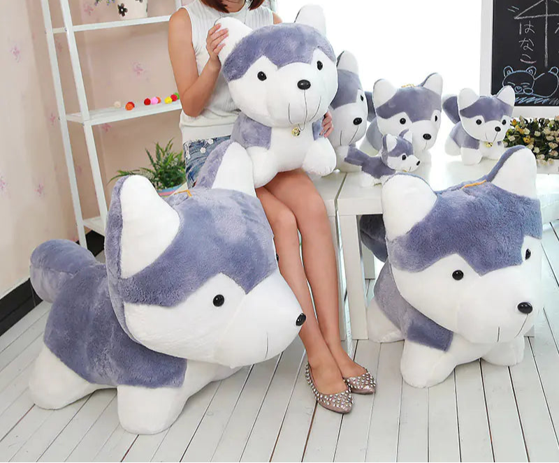 Woman sitting on a chair surrounded by large plush husky toys in a room.