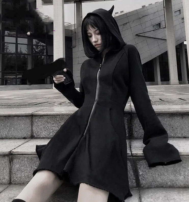 Person wearing a black hooded coat with devil horns sitting on steps outdoors.