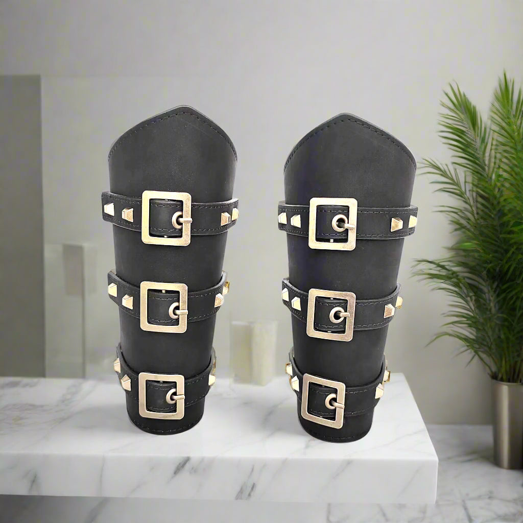Pair of black leather arm guards with gold buckles on a white background