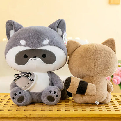 Two plush raccoons, one gray and white, the other brown, sitting on a yellow surface with a light background.