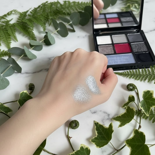Hand with silver glitter makeup swatch in front of a makeup palette