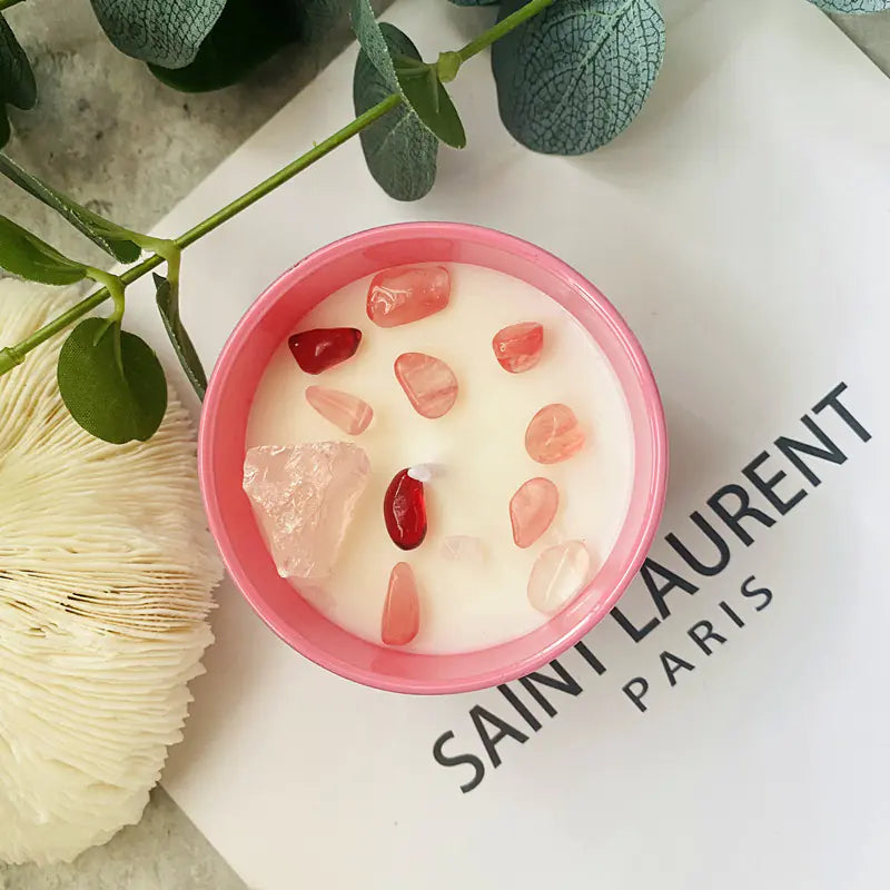 Candle in a pink container with decorative stones on a Saint Laurent Paris magazine