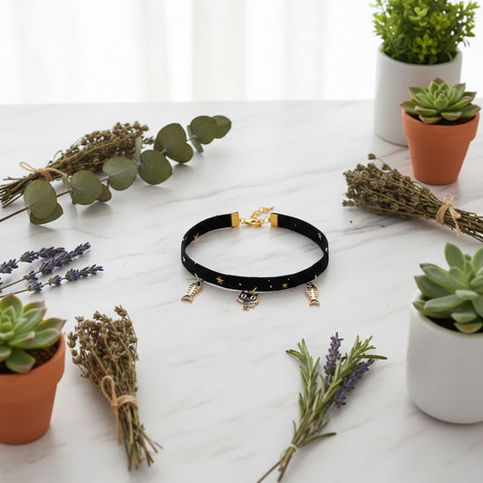 Black choker necklace with cat and fish charms on a pink background