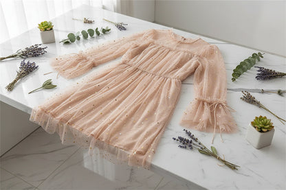 Person wearing a sheer pink dress with star patterns, sitting outdoors.