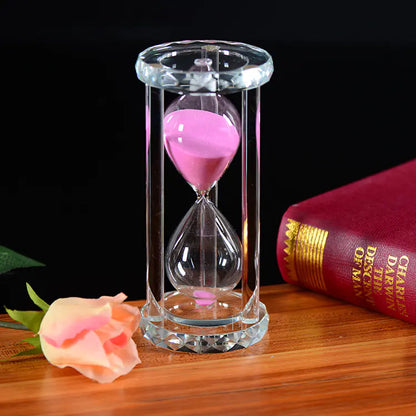 Sand timer with pink sand on a wooden surface next to a rose and a book.