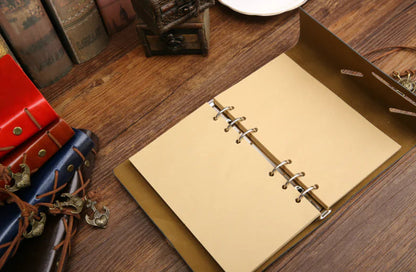 Beige notebook with metal rings on a wooden surface with decorative items.