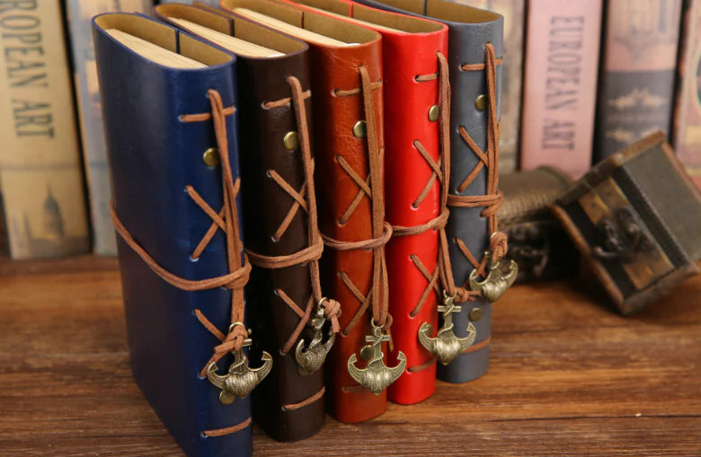 Set of leather-bound books with decorative straps on a wooden surface